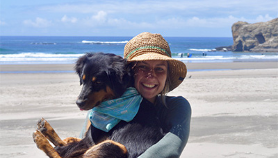 Kellie wearing a straw hat and long‑sleeved shirt smiles while holding a black‑a